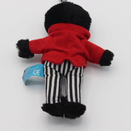 A small plush Golly doll or character keychain shown from the back, wearing a bright red fuzzy top, black-and-white vertically striped pants, and black fuzzy cuffs and feet, photographed on a plain light background. A blue tag is attached near the left side.