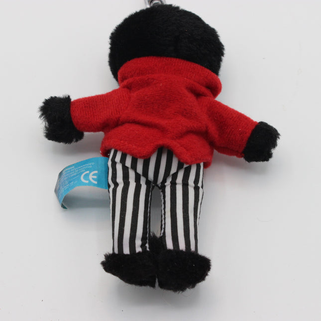 A small plush Golly doll or character keychain shown from the back, wearing a bright red fuzzy top, black-and-white vertically striped pants, and black fuzzy cuffs and feet, photographed on a plain light background. A blue tag is attached near the left side.
