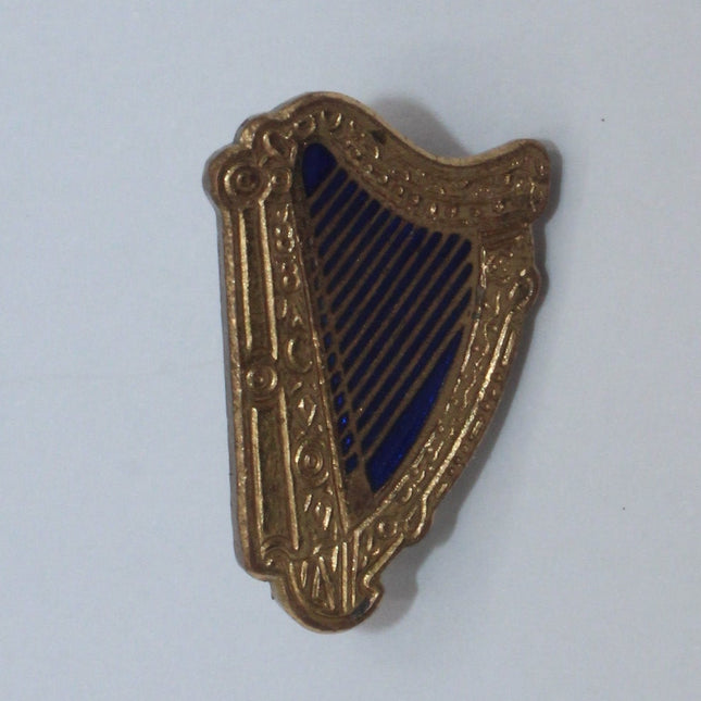 A small gold-toned harp-shaped pin or charm with dark navy blue string details, shown on a plain light gray background.