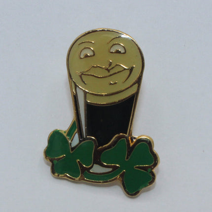 A small enamel pin shaped like a smiling beer mug with green shamrocks at the base, shown on a plain light background.