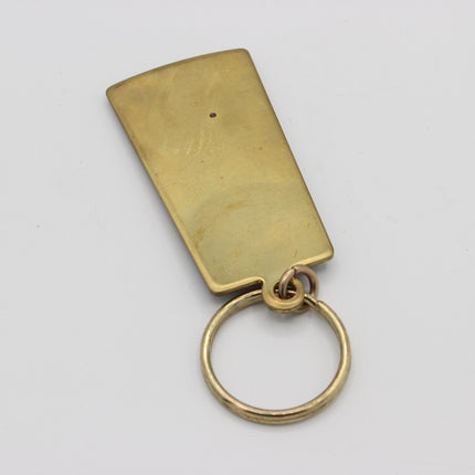 A blank brass Guinness keychain tag with a rectangular plate and a split key ring, shown on a plain light gray background.