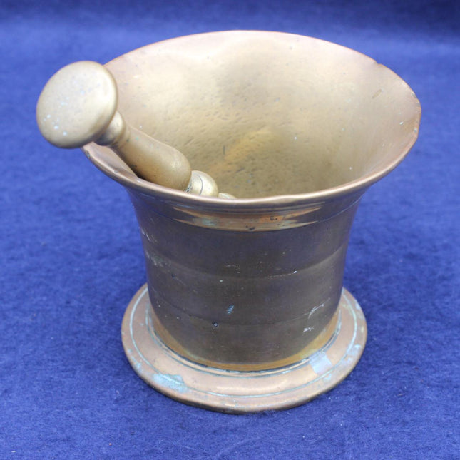 A vintage brass mortar and pestle set with a round base, shown on a textured blue background.