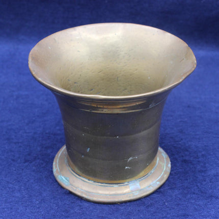 A vintage brass or bronze-colored metal cup with a flared rim and circular base, photographed against a textured blue background.