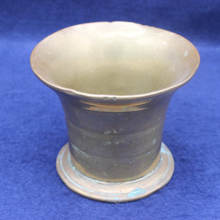 A vintage brass or bronze-colored metal cup with a flared rim and circular base, photographed against a textured blue background.