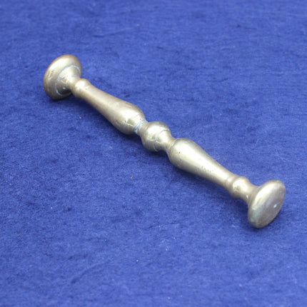 A vintage brass-toned metal bar with a turned, decorative center and round ends, photographed diagonally on a textured blue fabric background.