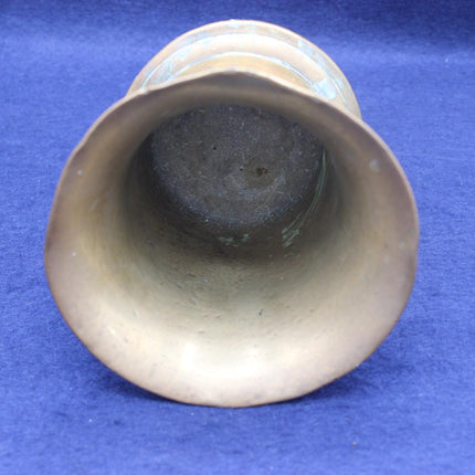 An antique brass bell-shaped vessel or cup shown from a top-down perspective, revealing a dark interior base, set against a textured blue background.