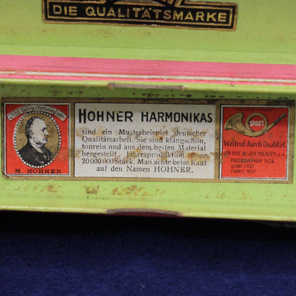 Close-up of a vintage Hohner Harmonika instrument showing the underside with a lime green painted body, pink inner edge, and two Hohner brand labels.