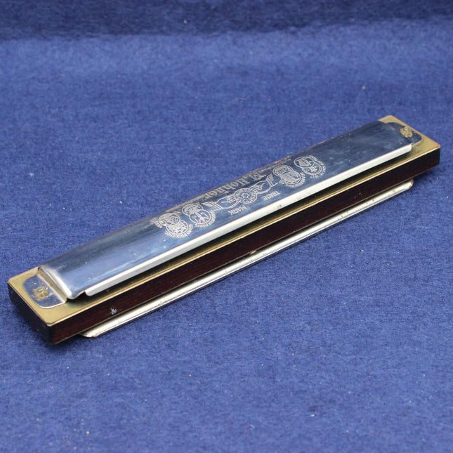 A vintage harmonica with a silver metal mouthpiece and brass body, resting on a textured blue fabric background.