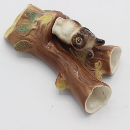 A ceramic owl figurine perched on a tree branch, photographed on a plain white background.