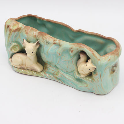 A ceramic planter shaped like a tree trunk with a glossy light green glaze and two small beige animal figurines nestled in the sides, photographed on a plain white background.