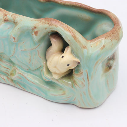 A ceramic planter shaped like a tree trunk with a small cream-colored fox figurine peeking out from the side, featuring a glossy light green glaze and brown distressed detailing, set against a plain white background.