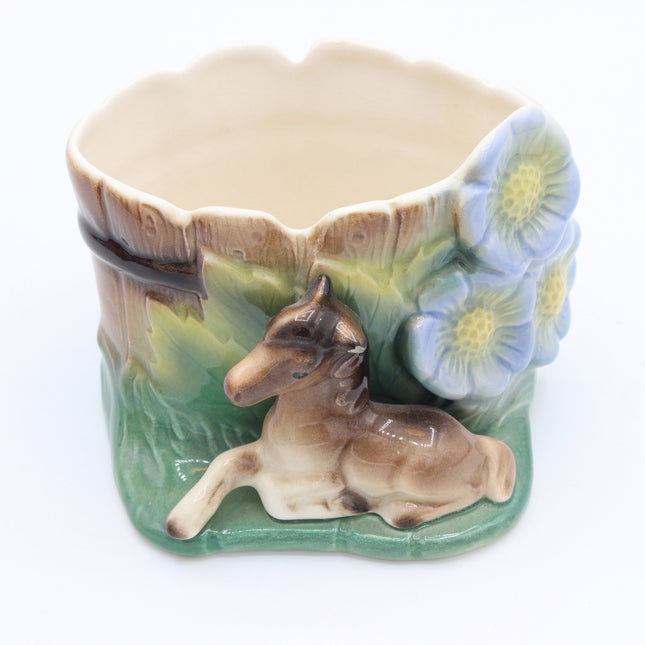 A vintage ceramic planter shaped like a tree trunk with a reclining deer and blue flowers, photographed on a white background.