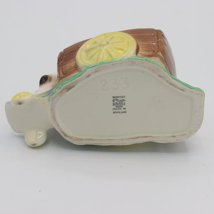 A vintage ceramic piggy bank shaped like a pig carrying a brown trunk with a yellow lemon design, photographed from underneath on a white background.