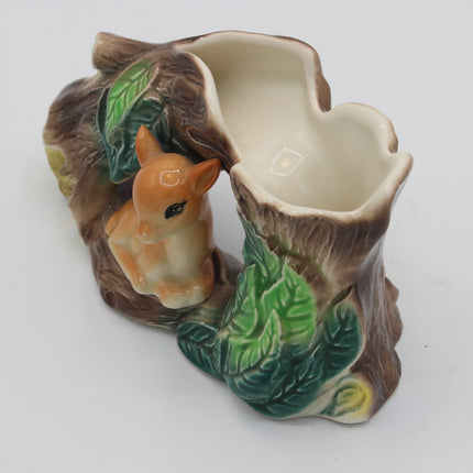 A ceramic tree stump planter with a small glazed fawn figurine, featuring green leaves and brown bark details on a white background.