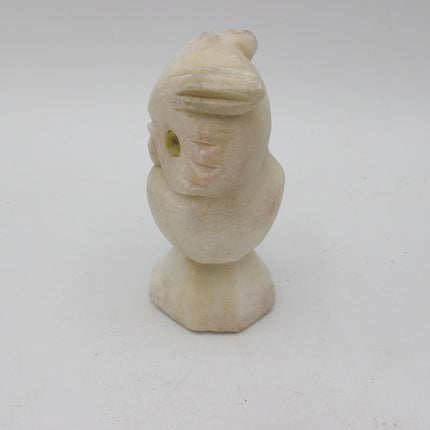 A small carved stone owl figurine in a warm cream or ivory tone, photographed against a plain light gray studio background.