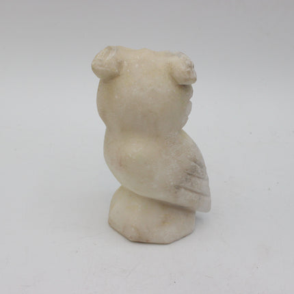 A small carved stone owl figurine in a warm cream or ivory tone, photographed against a plain light gray background.