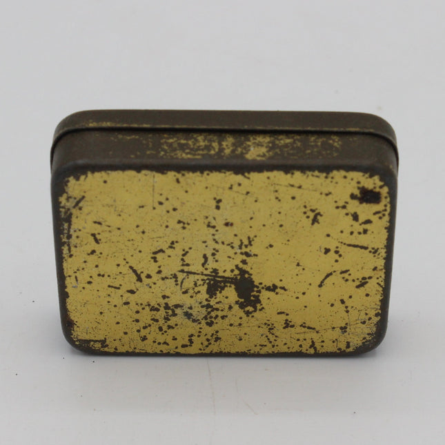 A small rectangular vintage tin with a distressed gold-colored lid and dark metal edges, photographed on a plain light gray background.