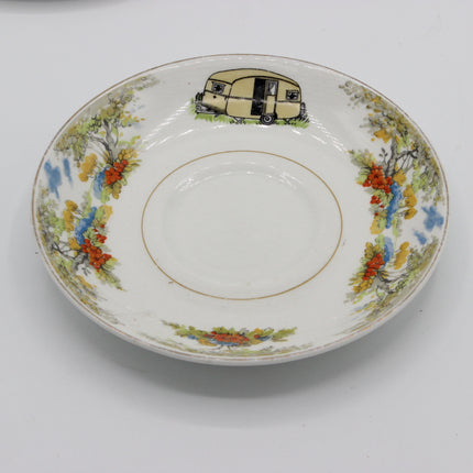 A vintage white porcelain plate or shallow dish featuring a hand-painted border with colorful floral motifs and a small illustrated camper trailer near the top edge.