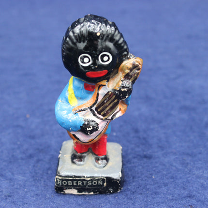 Figurine of a golliwog character holding a cricket bat on a blue background