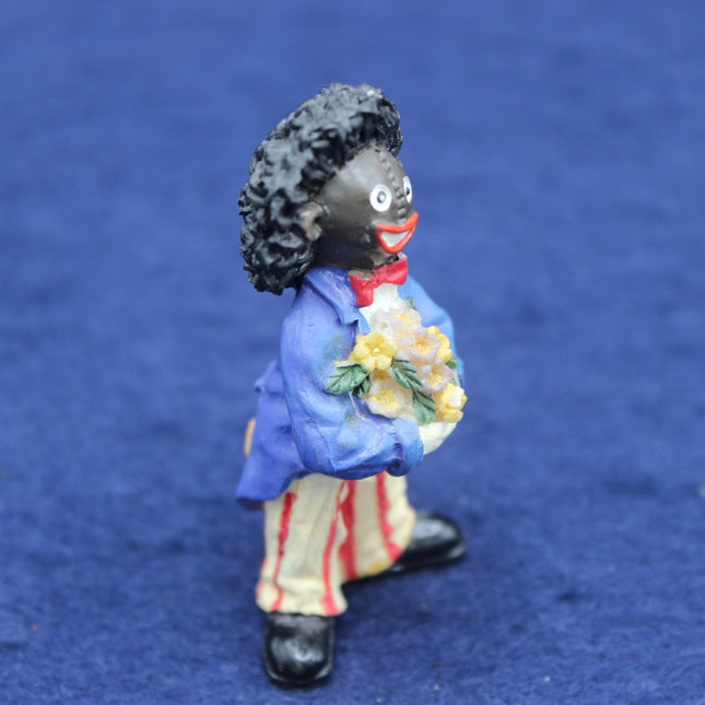 Figurine of a Golly in a blue coat holding flowers on a blue background