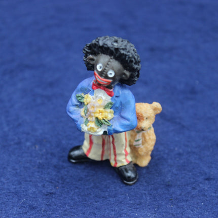Small Golly figurine of a person holding flowers and a teddy bear on a blue background