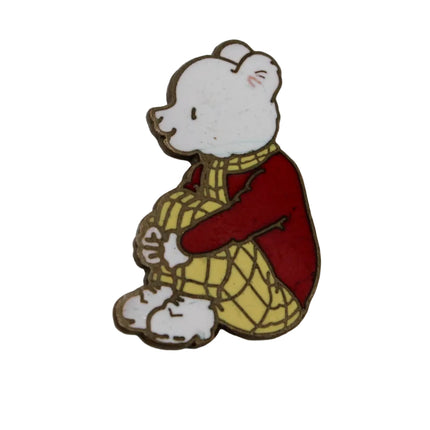 A small enamel pin of Rupert Bear wearing a red shirt and yellow plaid pants, shown on a plain light gray background.