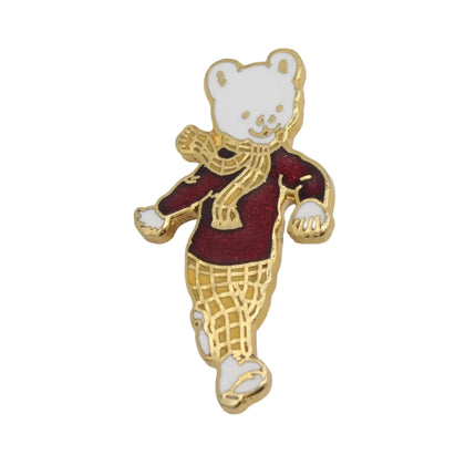 A small enamel pin Rupert bear wearing a burgundy sweater, gold scarf, and gold plaid pants, shown on a plain light background.