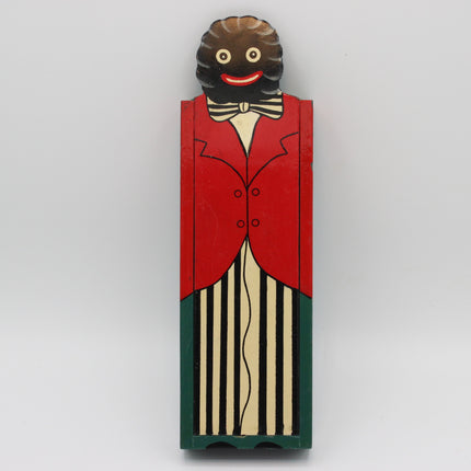 A vintage hand-painted wooden box with Golly figure, featuring a brown wig, red jacket, cream shirt, black-and-cream striped pants, and a black bow tie, set against a plain light gray background.