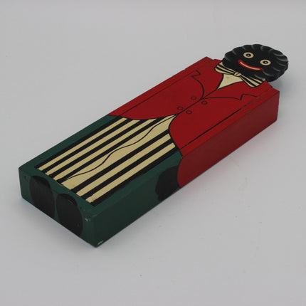 A hand-painted wooden pencil box featuring a Golly in a red jacket and striped trousers, with a black face and black hair protruding from the top, photographed on a light gray background.