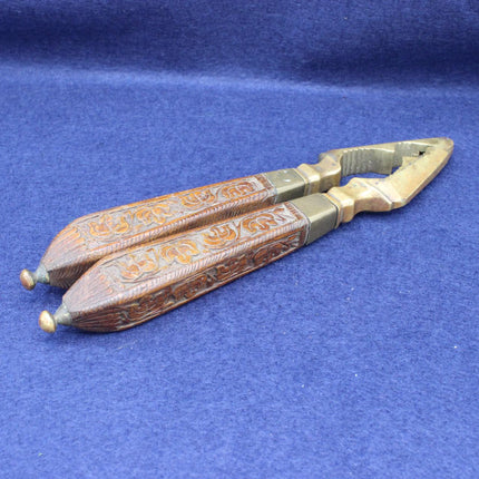 A pair of ornate metal and wood-handled nutcrackers with carved brown handles and brass-toned ends, photographed on a textured blue fabric background.