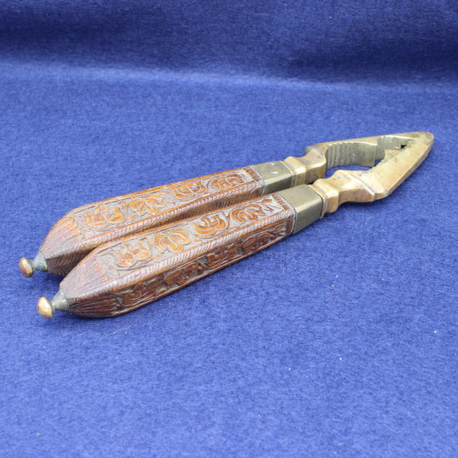 A pair of ornate metal and wood-handled nutcrackers with carved brown handles and brass-toned ends, photographed on a textured blue fabric background.