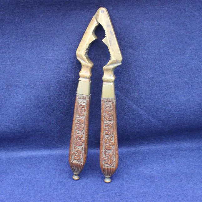 Vintage metal nutcracker with ornate carved brown handles and gold-toned metal head, standing upright on a blue textured fabric background.