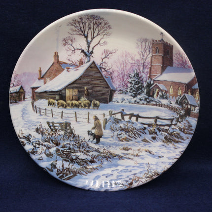 Decorative plate with a winter scene of a village, featuring houses, trees, and a person with a dog.