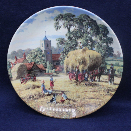 Decorative plate with a rural scene featuring a church, hay bales, and people working in a field.