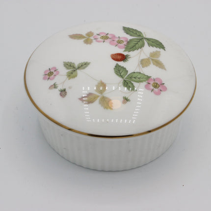 A round white porcelain keepsake box with a lid, decorated with pink strawberries, green leaves, and a thin gold rim, set against a plain white background.