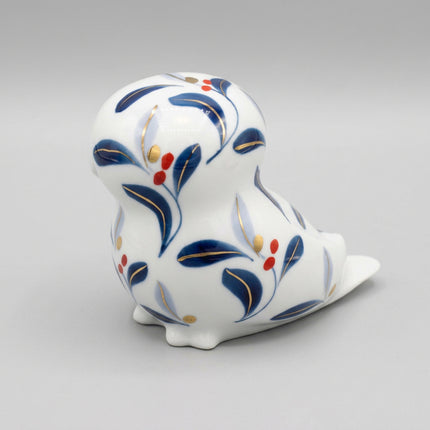 A white ceramic bird figurine decorated with blue floral patterns, gold outlines, and small red berries, photographed on a clean white background.