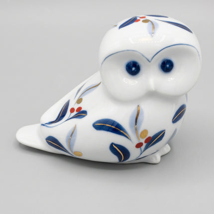 A white ceramic owl figurine decorated with blue, gold, and red floral patterns, photographed on a seamless white background.