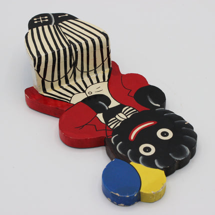 A vintage hand-painted wooden toy Golly figure, ffeaturing a black body with red clothing, a black-and-white striped hat, and separate painted pieces in blue and yellow.