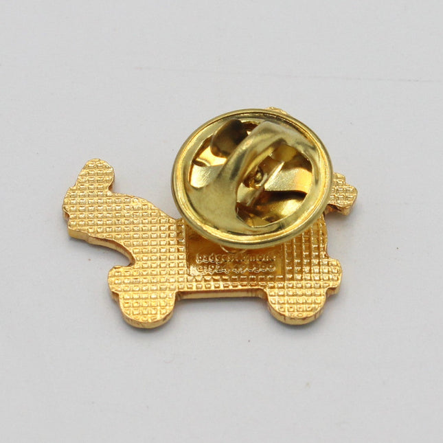 A small gold-colored metal pin or badge with a textured base and a shiny circular top, photographed on a plain light background.
