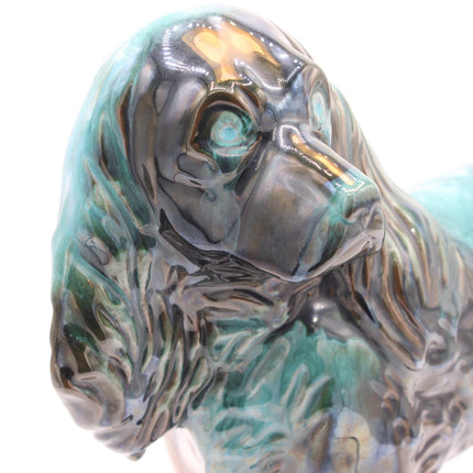 Close-up of a glossy ceramic dog figurine with a dark charcoal body and turquoise-green glazed highlights, shown against a plain white background.