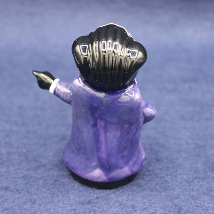 Small figurine of a Golly in a purple outfit and black hat on a blue background