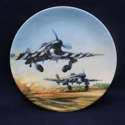 Decorative plate with a painting of two fighter jets on a runway and in the sky.