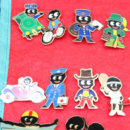 A collection of colorful Golly enamel lapel pins featuring Robertsons jam characters with black skin and various colorful outfits, displayed on a bright red felt Golly scroll.