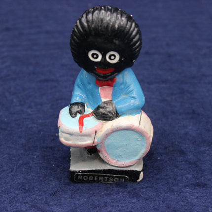 Figurine of a Golly with a large black hairstyle, wearing a blue outfit and pink shoes, on a blue background.