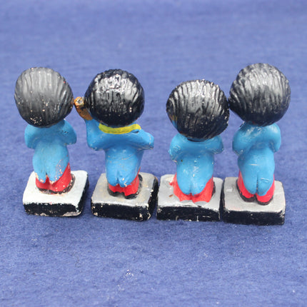 Four small golly figurines with blue bodies, black hair, and red shoes on a blue background