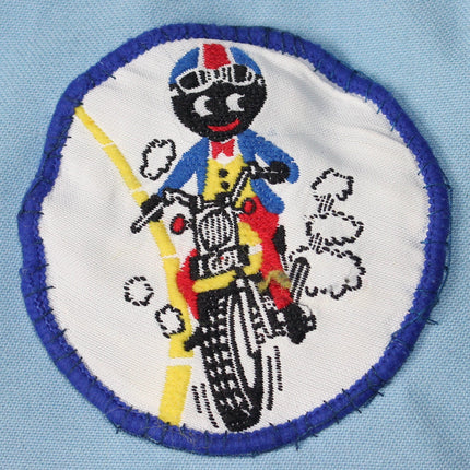 Patch of a Golly riding a motorcycle on a light blue fabric background
