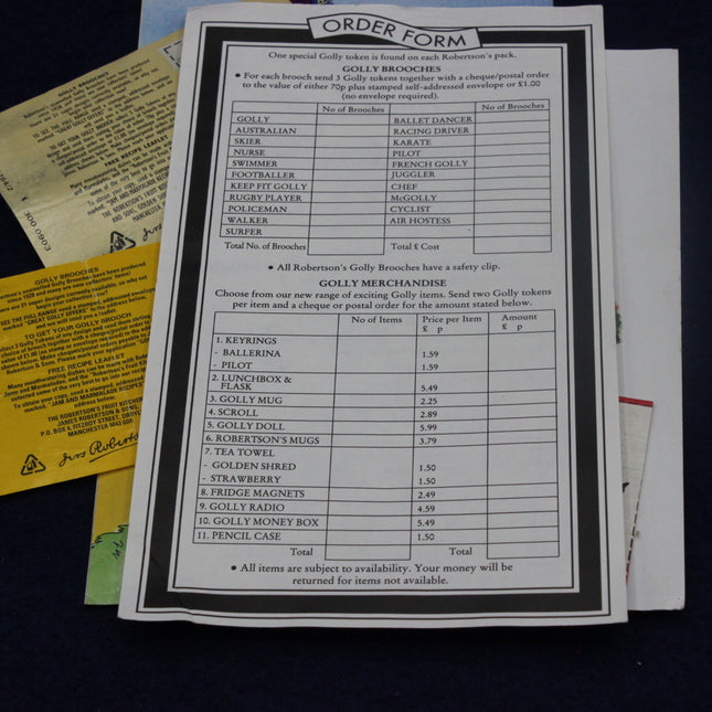 Order form for Golly brooches and merchandise on a dark surface with other documents.