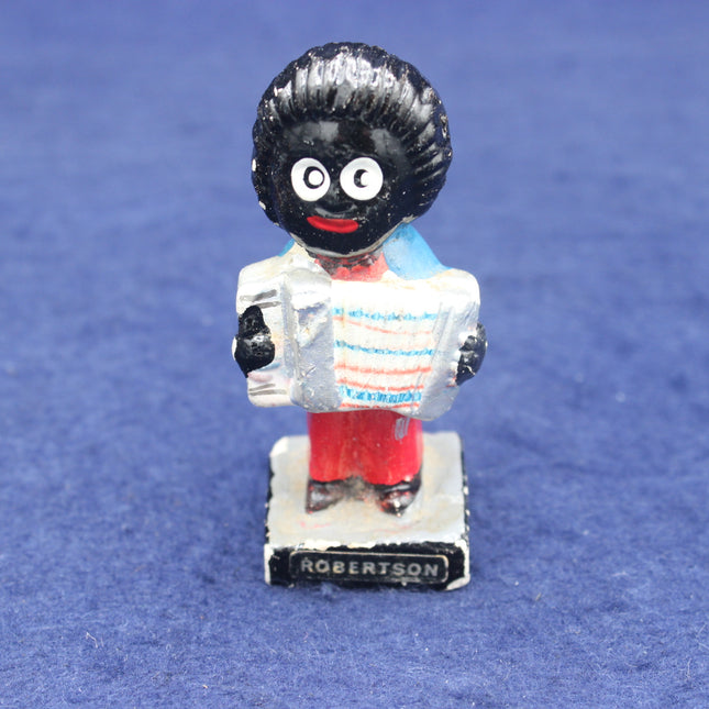 Vintage toy figure with a black face, white shirt, red pants, and 'Robertson' branding on a blue background.