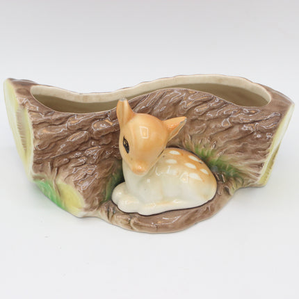 A ceramic planter shaped like a tree stump with a small fawn figurine sitting inside, photographed on a plain white background.