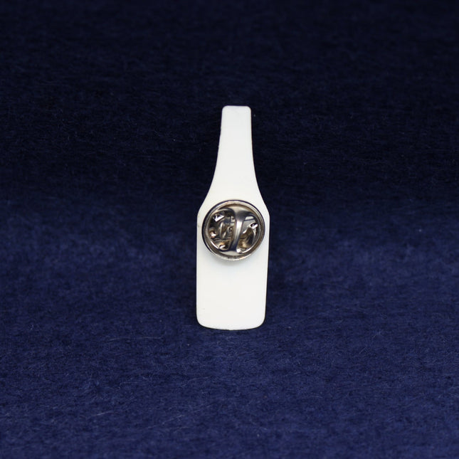 White Malibu bottle-shaped pin badge with a circular clasp on a dark blue textured background